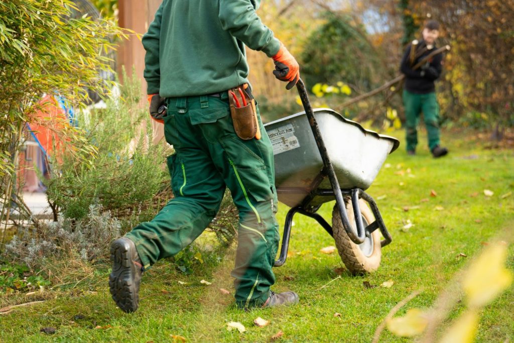 man in green gardening clothes pushing wheelbarrow through garden