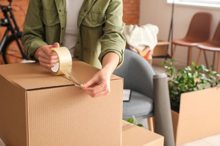 woman taping top of cardboard box shut